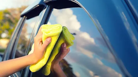 Kvinne pusser bilvindu med mikrofiberklut